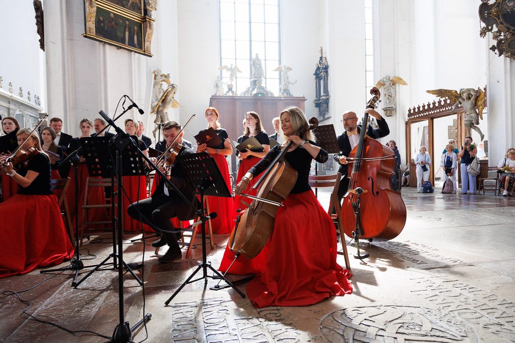 Zespół Cappella Gedanensis podczas występu w Bazylice Mariackiej w Gdańsku, z instrumentalistami w czerwonych strojach.