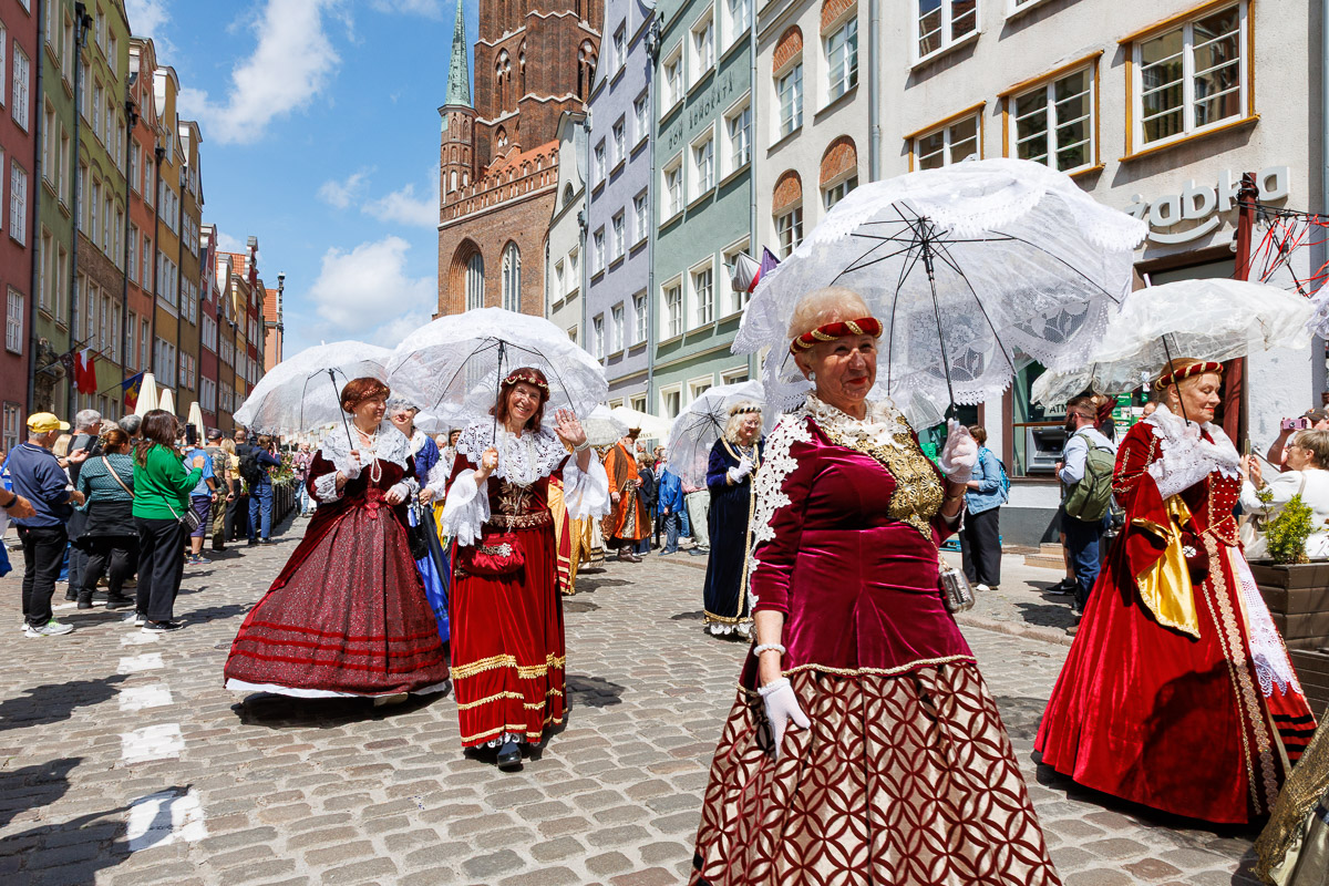 Barwny korowód uczestników w historycznych strojach podczas plenerowego wydarzenia kulturalnego na ulicach Gdańska.