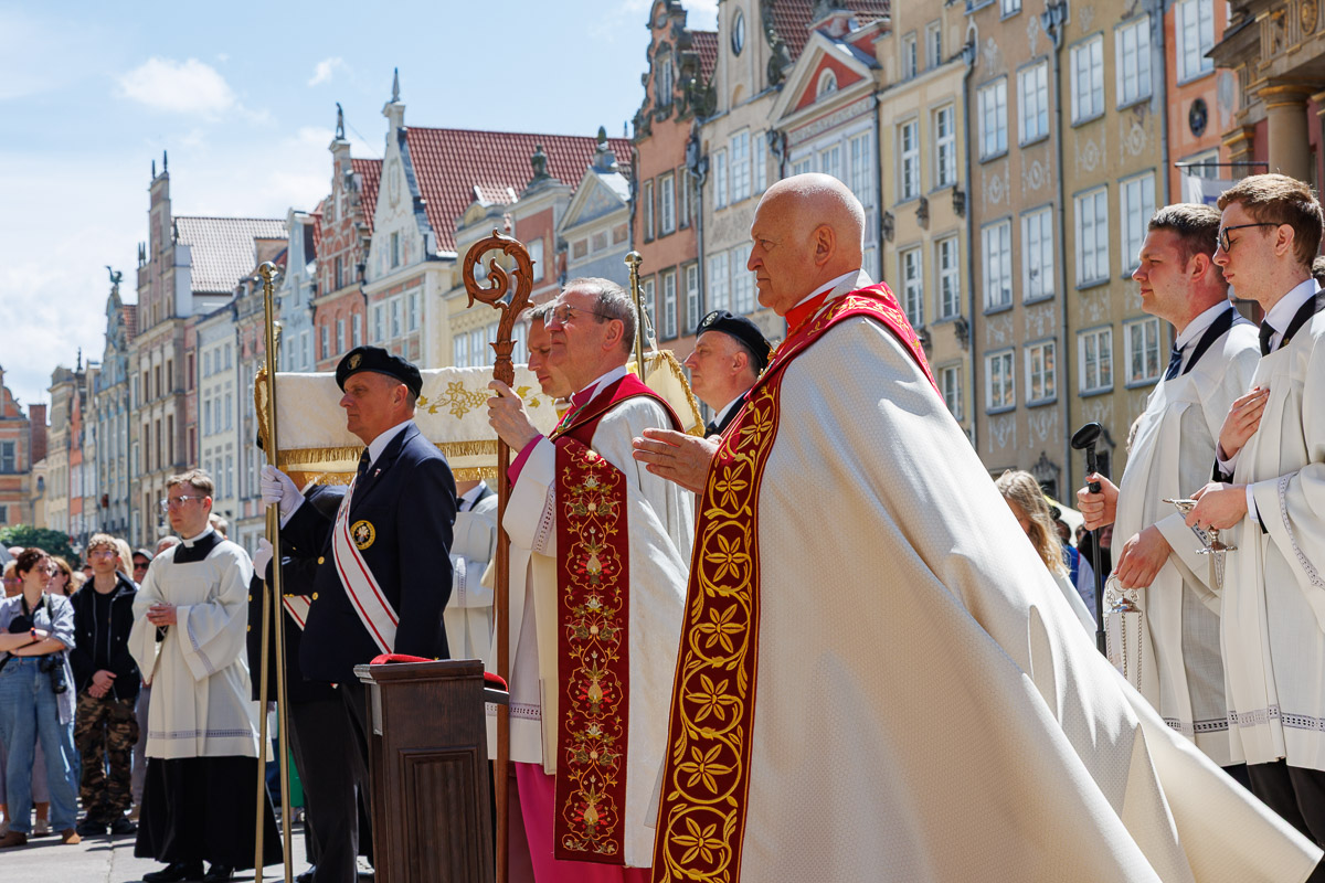 Arcybiskup Tadeusz Wojda podczas uroczystej procesji religijnej na ulicach Gdańska, w otoczeniu duchowieństwa i uczestników ceremonii.