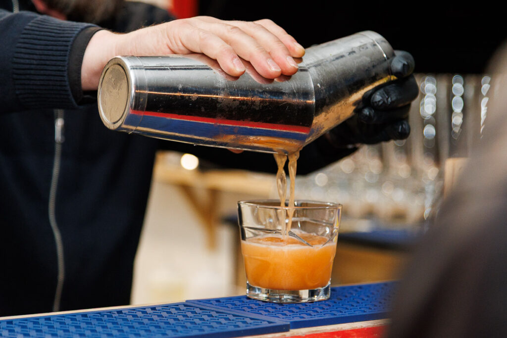 Barman nalewający przygotowany koktajl z metalowego shakera do szklanki podczas wydarzenia.